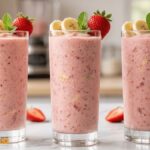Fresh homemade strawberry banana smoothie in a clear glass topped with fresh strawberries, banana slices, and mint leaves.