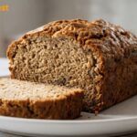 Freshly baked homemade banana bread with a golden crust and moist sliced interior served on a white plate.