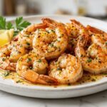 Garlic butter shrimp served on a white plate with a rich buttery garlic sauce, fresh parsley, and lemon wedges.