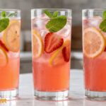 Refreshing homemade strawberry lemonade served in a tall glass with fresh strawberry slices, lemon slices, ice cubes, and mint leaves.