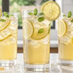 Fresh homemade lemonade served in a clear glass with lemon slices, mint leaves, and ice cubes on a white marble countertop.