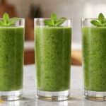 Healthy green smoothie in a clear glass made with spinach, banana, avocado, and kiwi, served on a white marble countertop.
