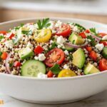 Healthy quinoa salad with avocado, cherry tomatoes, cucumber, red onion, parsley, feta cheese, and tri-color quinoa in a white bowl.