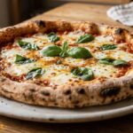 Homemade pizza with a crispy golden crust, melted mozzarella cheese, fresh basil, and tomato sauce served on a white plate.